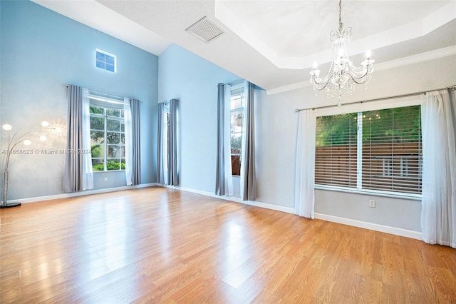 spare room featuring light wood-type flooring, a wealth of natural light, a tray ceiling, and an inviting chandelier