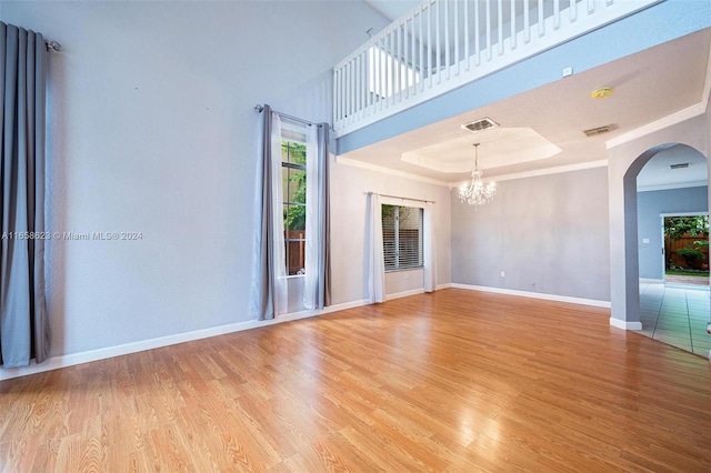 unfurnished living room with light wood-type flooring, a chandelier, and a raised ceiling