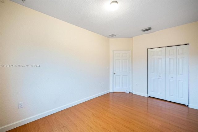 unfurnished bedroom with a textured ceiling, hardwood / wood-style floors, and a closet