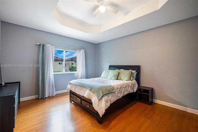 bedroom featuring ceiling fan, a raised ceiling, and light hardwood / wood-style flooring