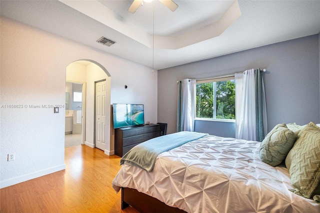 bedroom with light wood-type flooring, a tray ceiling, ceiling fan, and a closet