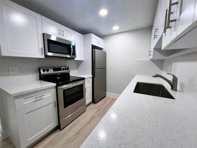 kitchen with white cabinets, light stone counters, appliances with stainless steel finishes, light hardwood / wood-style floors, and sink