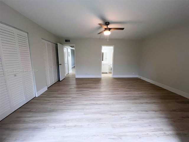 unfurnished bedroom featuring multiple closets, light wood-type flooring, and ceiling fan