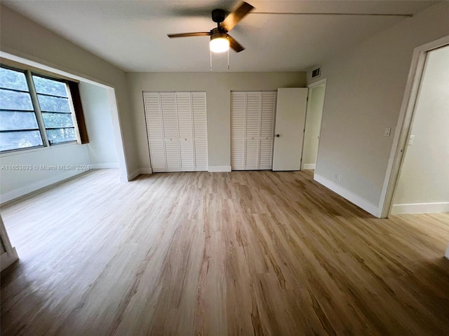 unfurnished bedroom featuring two closets, light wood-type flooring, and ceiling fan