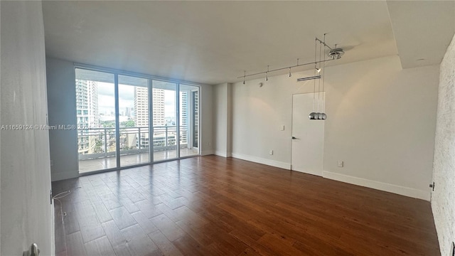 empty room featuring dark wood-type flooring, rail lighting, and a wall of windows