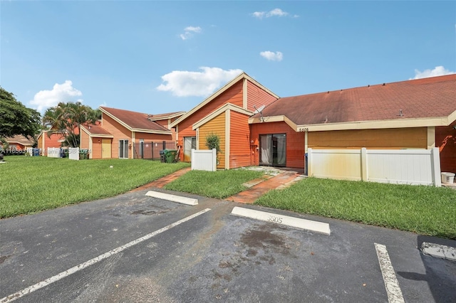 view of front of property with uncovered parking, fence, and a front lawn