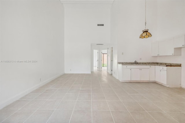 kitchen featuring light tile patterned floors, hanging light fixtures, sink, white cabinetry, and a towering ceiling