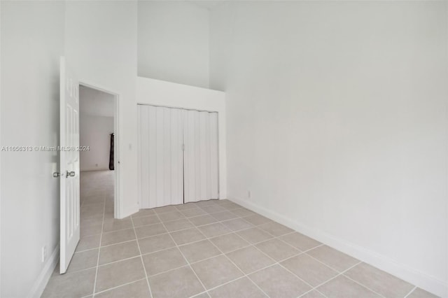 empty room featuring light tile patterned floors, a towering ceiling, and baseboards