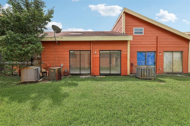 rear view of house with central air condition unit and a lawn