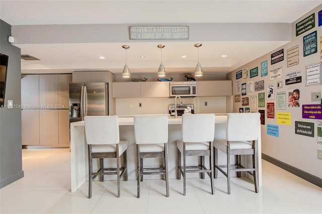 kitchen with hanging light fixtures, a kitchen bar, gray cabinetry, appliances with stainless steel finishes, and light tile patterned flooring