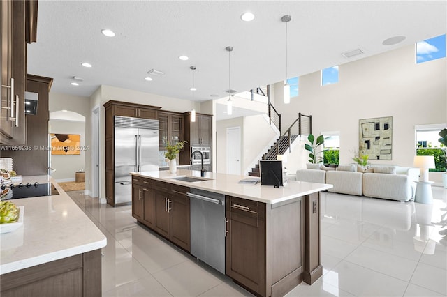 kitchen featuring a kitchen island with sink, stainless steel appliances, sink, pendant lighting, and a textured ceiling