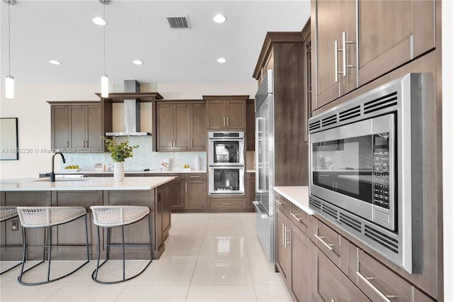 kitchen featuring appliances with stainless steel finishes, light tile patterned flooring, sink, an island with sink, and hanging light fixtures