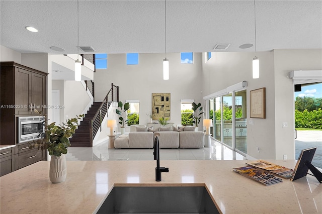 5458 E Stillwater Shores Dr, Davie, FL 33314 - kitchen featuring stainless steel microwave, dark brown cabinetry, hanging light fixtures, light stone counters, and a textured ceiling