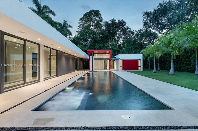 pool at dusk featuring an outbuilding and a lawn