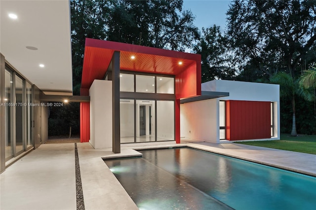 pool at dusk with a patio area and an outdoor structure