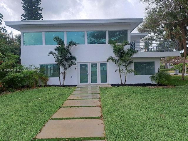 exterior space featuring a balcony, a front lawn, and stucco siding