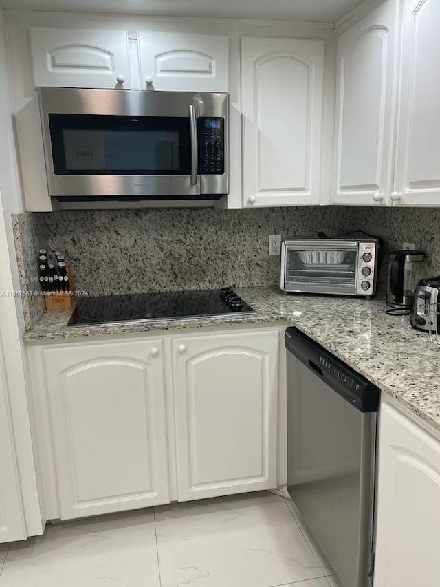 kitchen featuring light stone counters, appliances with stainless steel finishes, white cabinets, and decorative backsplash