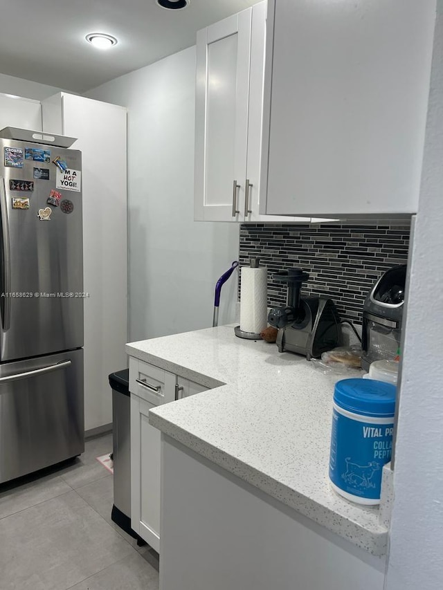 kitchen with stainless steel fridge, backsplash, white cabinets, and light stone countertops