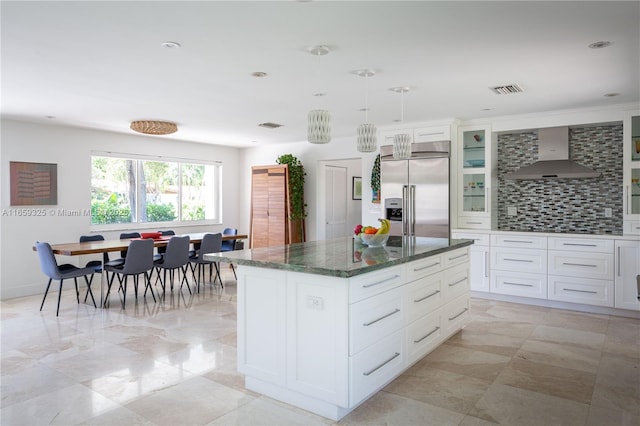 kitchen featuring glass insert cabinets, white cabinets, a kitchen island, built in refrigerator, and wall chimney exhaust hood