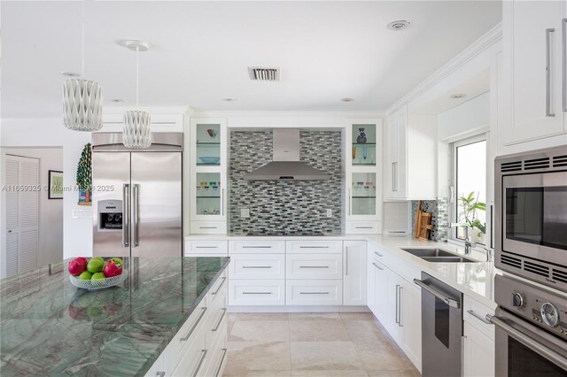 kitchen featuring wall chimney range hood, white cabinets, dark stone counters, built in appliances, and a center island