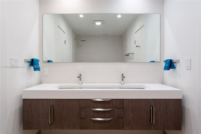 full bath with tasteful backsplash, tiled shower, a sink, and double vanity