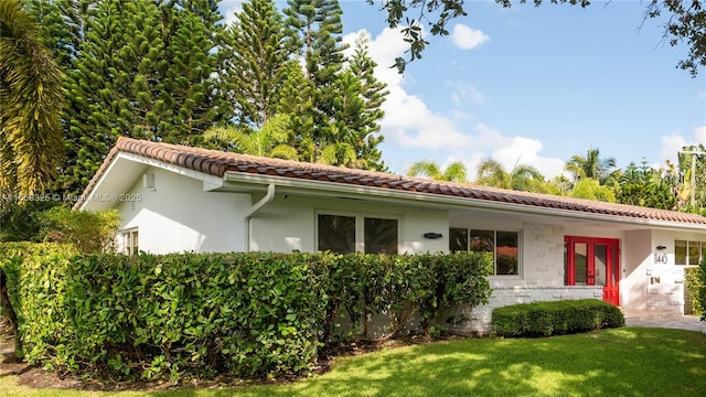 view of front of home with stone siding, a tile roof, a front lawn, and stucco siding