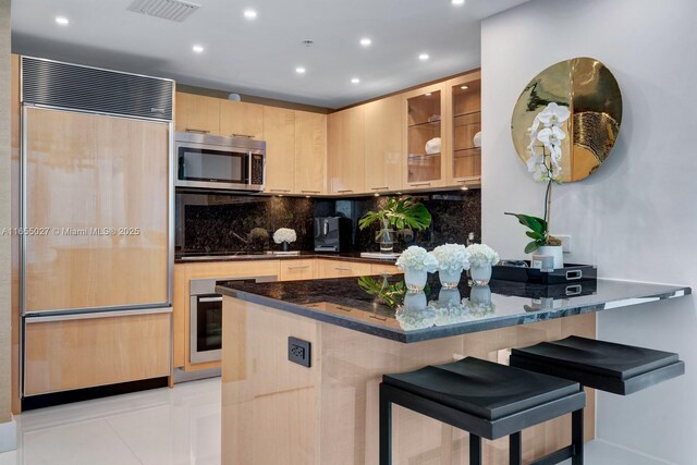 kitchen featuring a breakfast bar, kitchen peninsula, light brown cabinets, and appliances with stainless steel finishes