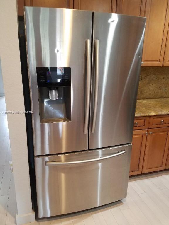 room details featuring stainless steel refrigerator with ice dispenser, light hardwood / wood-style floors, decorative backsplash, and light stone counters