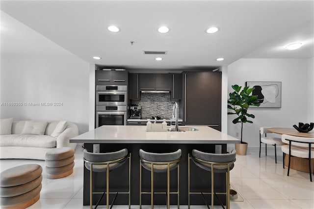 kitchen with stainless steel double oven, an island with sink, a breakfast bar area, and sink