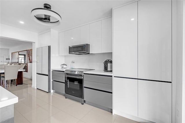 kitchen featuring appliances with stainless steel finishes, ceiling fan, light tile patterned floors, and white cabinets