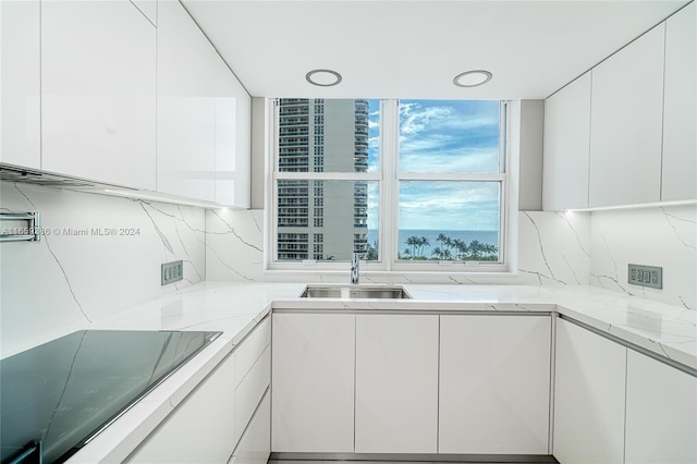 kitchen with white cabinets, stovetop, light stone countertops, sink, and tasteful backsplash