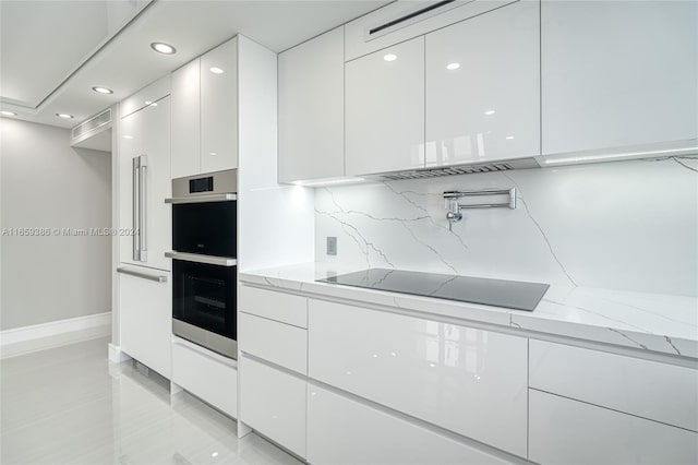 kitchen featuring stainless steel double oven, light stone counters, decorative backsplash, and white cabinets