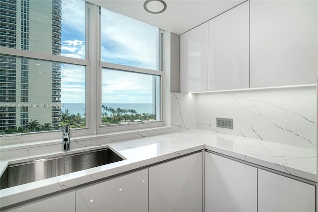 kitchen with a water view, light stone counters, sink, and white cabinets