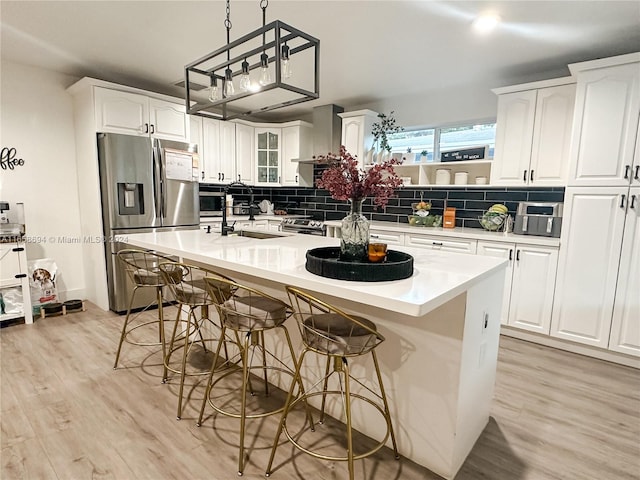 kitchen with an island with sink, appliances with stainless steel finishes, white cabinets, and wall chimney exhaust hood