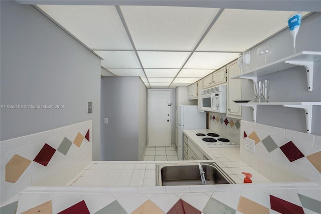 kitchen with white appliances, light tile patterned floors, tile counters, sink, and decorative backsplash