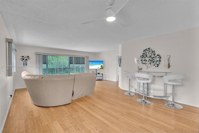 living room with light wood-type flooring, ceiling fan, and a textured ceiling