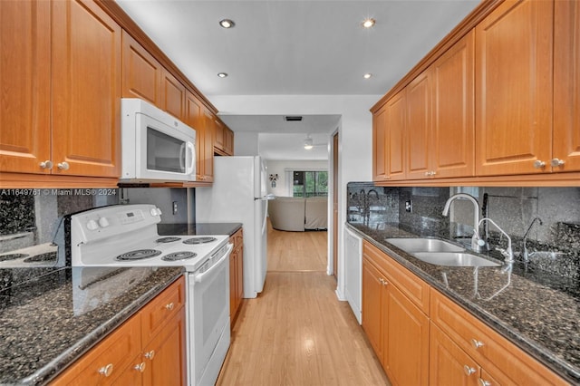 kitchen featuring light hardwood / wood-style flooring, white appliances, dark stone countertops, and sink