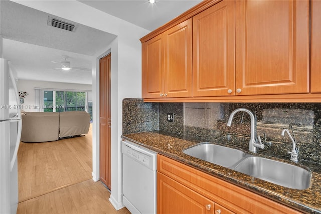 kitchen with light wood-type flooring, white appliances, sink, dark stone counters, and ceiling fan