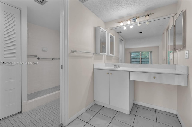 bathroom featuring tiled shower, vanity, tile patterned flooring, and a textured ceiling