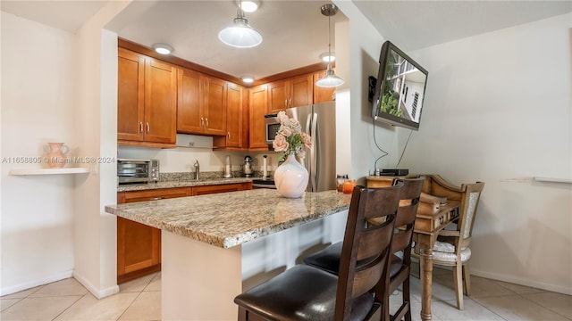 kitchen featuring light stone counters, decorative light fixtures, a kitchen bar, light tile patterned floors, and appliances with stainless steel finishes