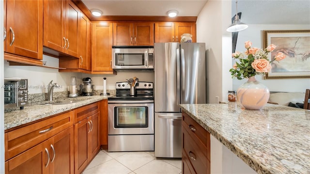 kitchen with light stone countertops, appliances with stainless steel finishes, hanging light fixtures, and sink