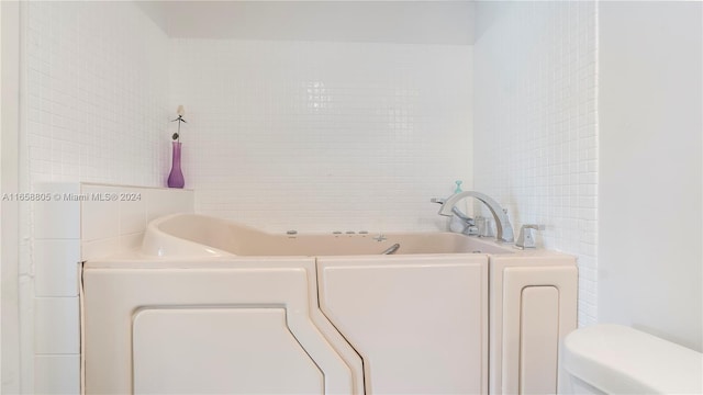 bathroom with a bath, washer / clothes dryer, toilet, and tile walls