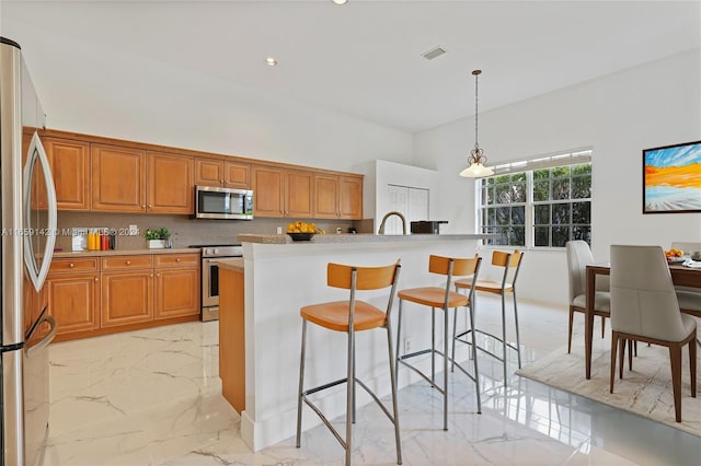 kitchen featuring appliances with stainless steel finishes, decorative backsplash, an island with sink, a breakfast bar area, and pendant lighting