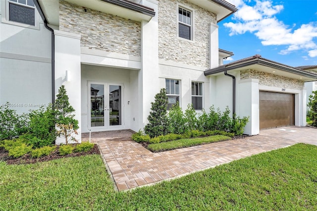 view of exterior entry with french doors, a lawn, and a garage