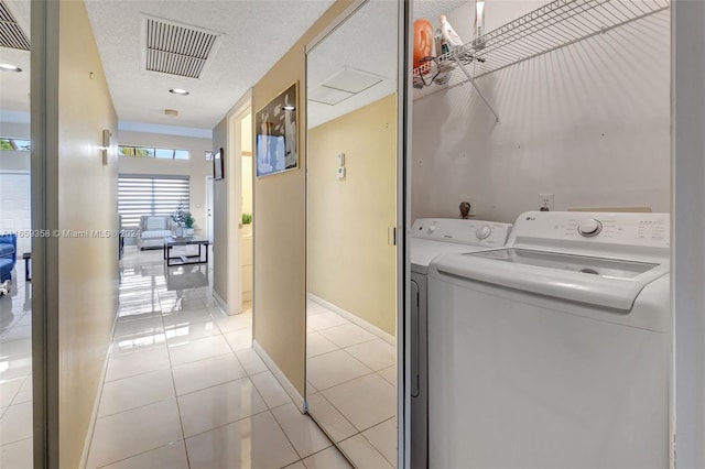 washroom with a textured ceiling, washing machine and dryer, and light tile patterned floors