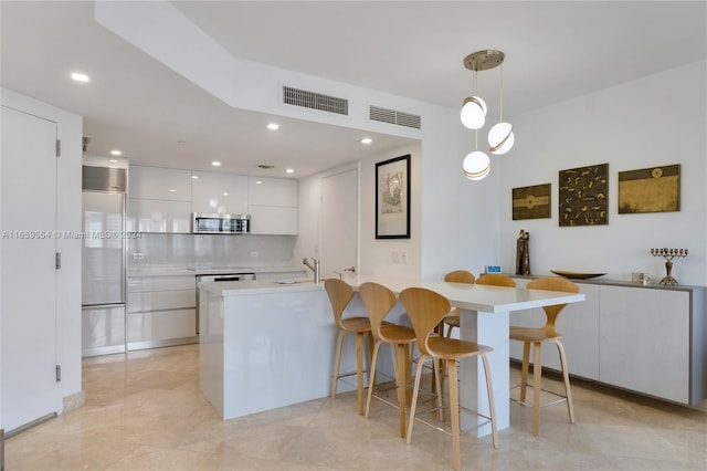 kitchen with white cabinets, hanging light fixtures, sink, kitchen peninsula, and a breakfast bar