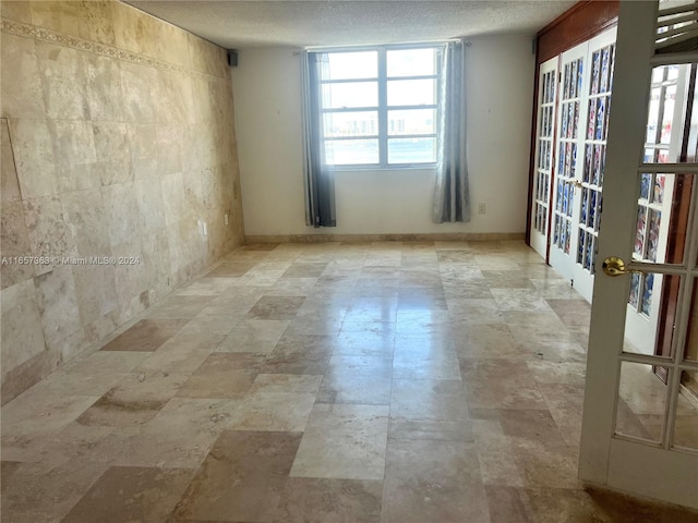 unfurnished room with tile walls, a textured ceiling, and french doors