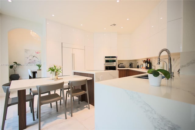 kitchen featuring stainless steel double oven, kitchen peninsula, white cabinetry, and sink