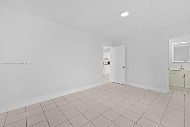 unfurnished room featuring light tile patterned floors, a textured ceiling, and sink