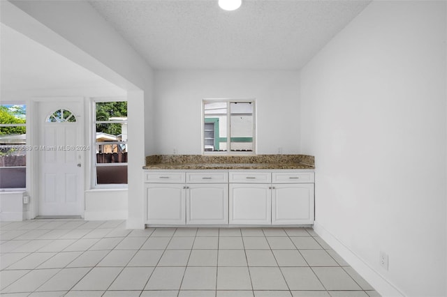 kitchen with dark stone countertops, white cabinetry, a textured ceiling, and light tile patterned floors